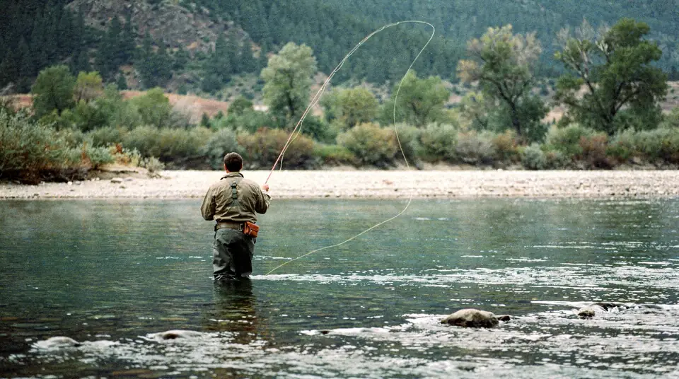 An angler seen from behind fly fishing a clear mountain stream